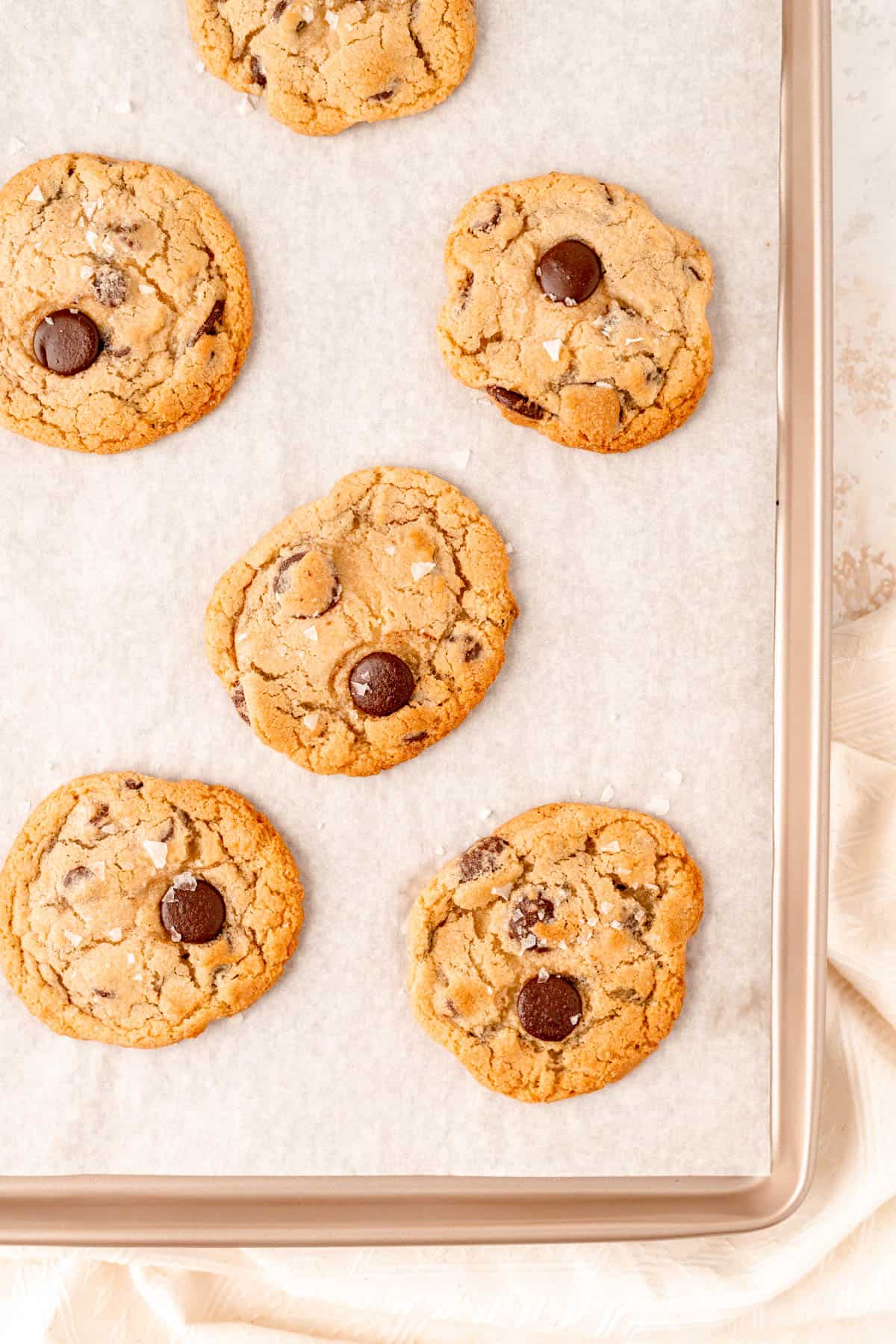 baked and settled salted chocolate chip cookies on a gold cookie sheet.