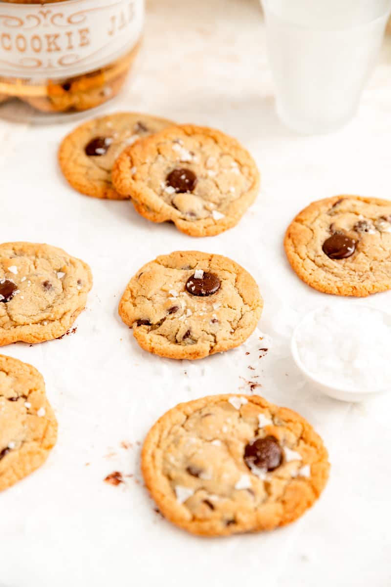 salted chocolate chip cookies laying on parchment with a bowl of sea salt