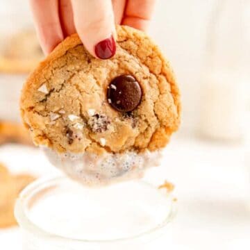 a close up of a chocolate chip cookie with a hand having just dunked it in milk