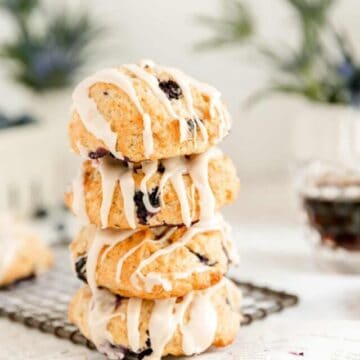 a stack of 4 blueberry scones on a dark wire rack with flowers and syrup pitcher