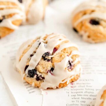 close up of a glazed maple blueberry scone on torn out recipe pages.