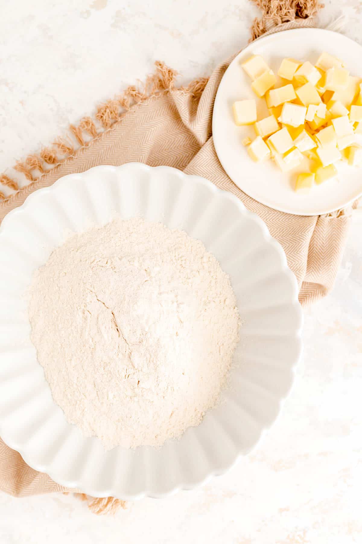 a bowl of dry ingredients and a small plate of cold butter cubes on a brown towel