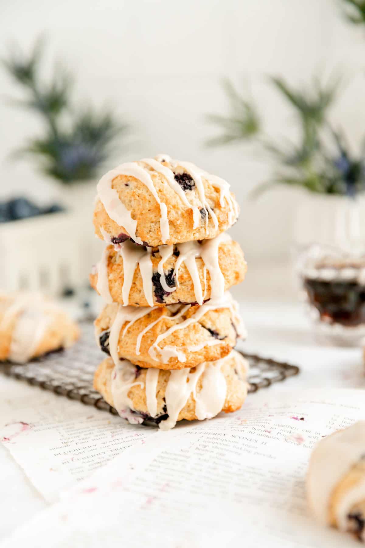 a stack of 4 blueberry scones on a dark wire rack with flowers and syrup pitcher