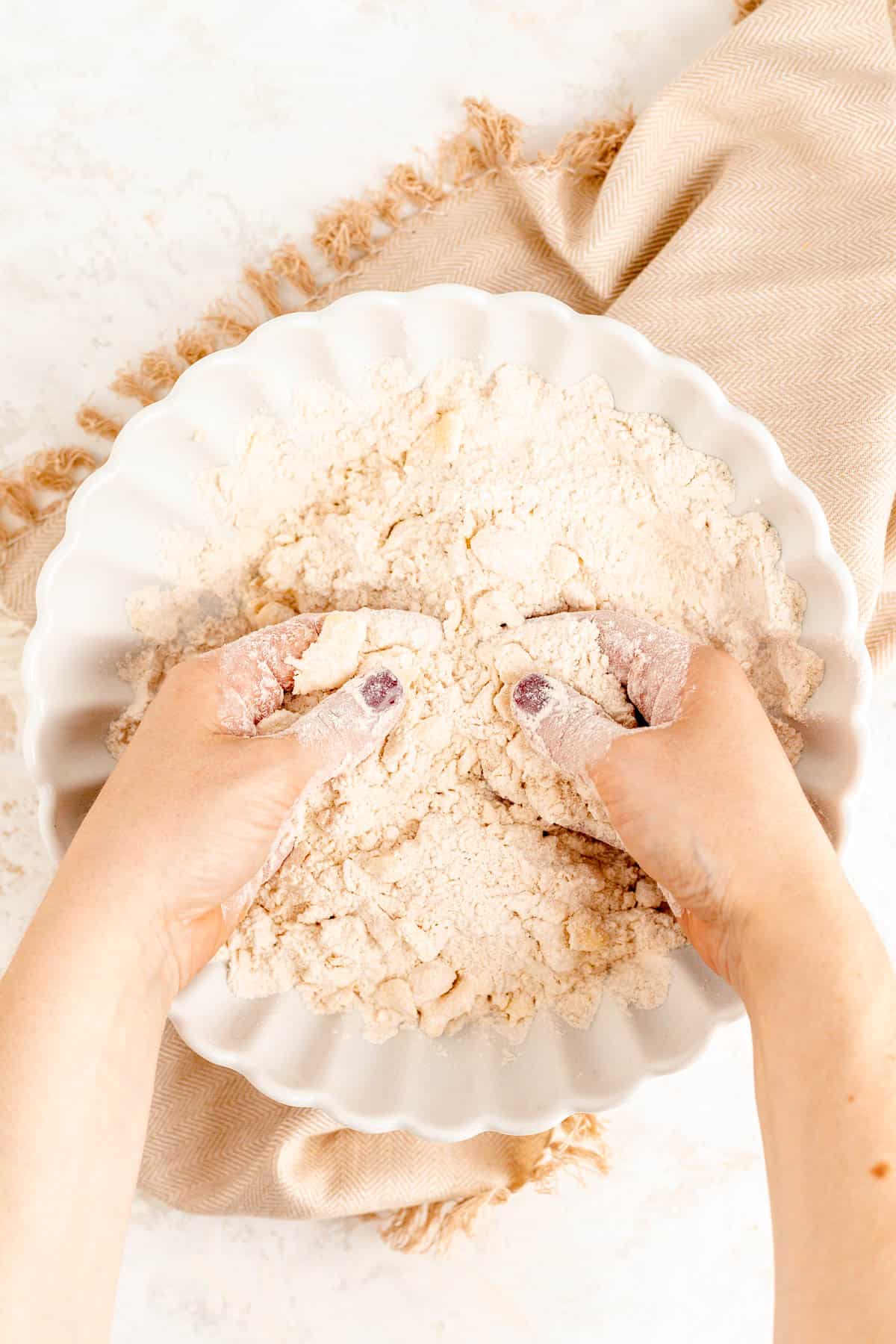 two hands smearing cold butter pieces into a mix of dry ingredients