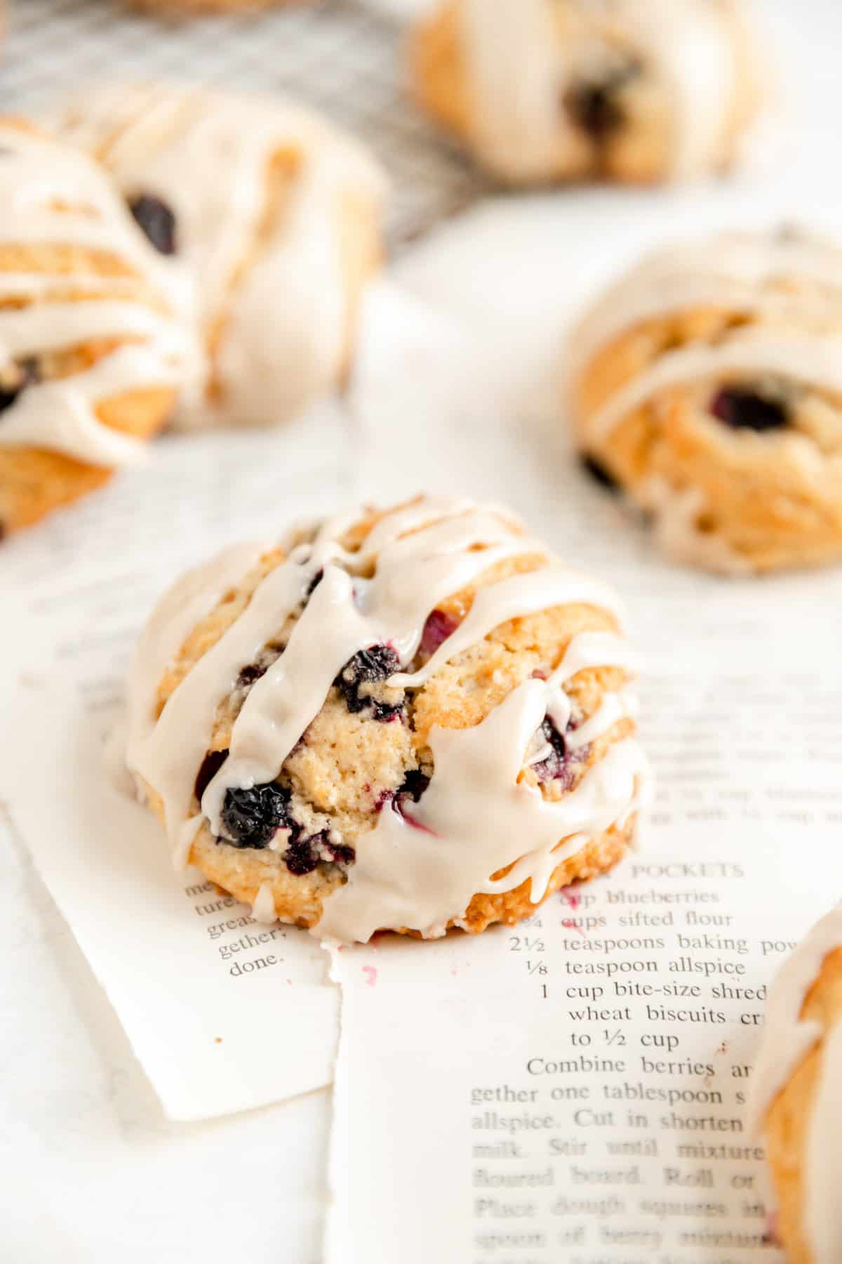 close up of a glazed maple blueberry scone on torn out recipe pages