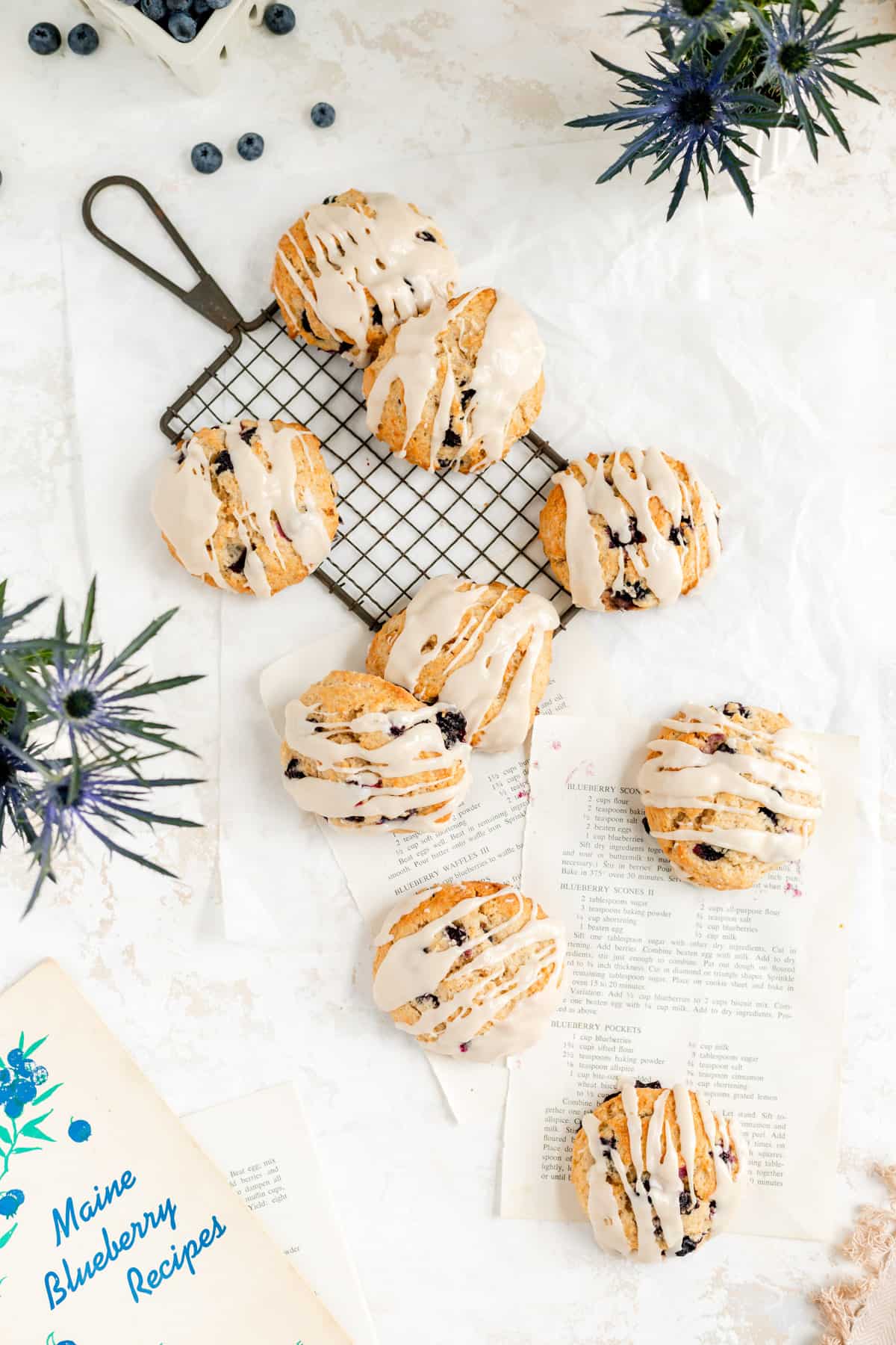 glazed scones on a wire rack and recipe pages from above with blue flowers and berries