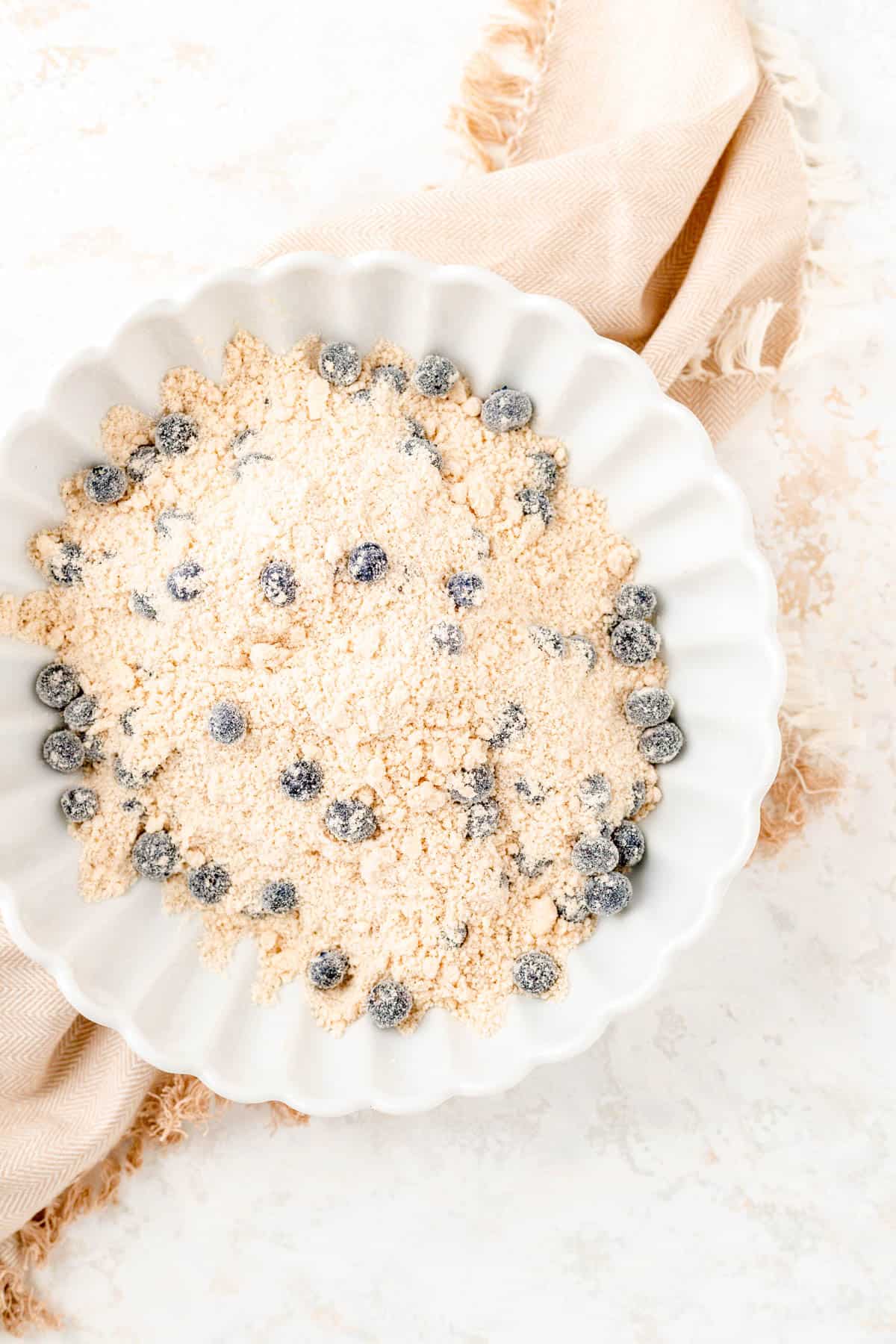 dry ingredients with butter cut in and blueberries as well in a white bowl