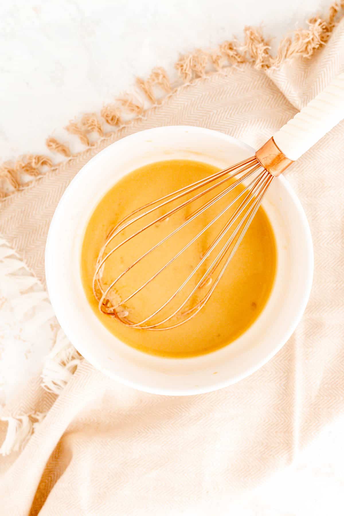 the wet ingredients for scones mixed in a white bowl with a copper whisk in it