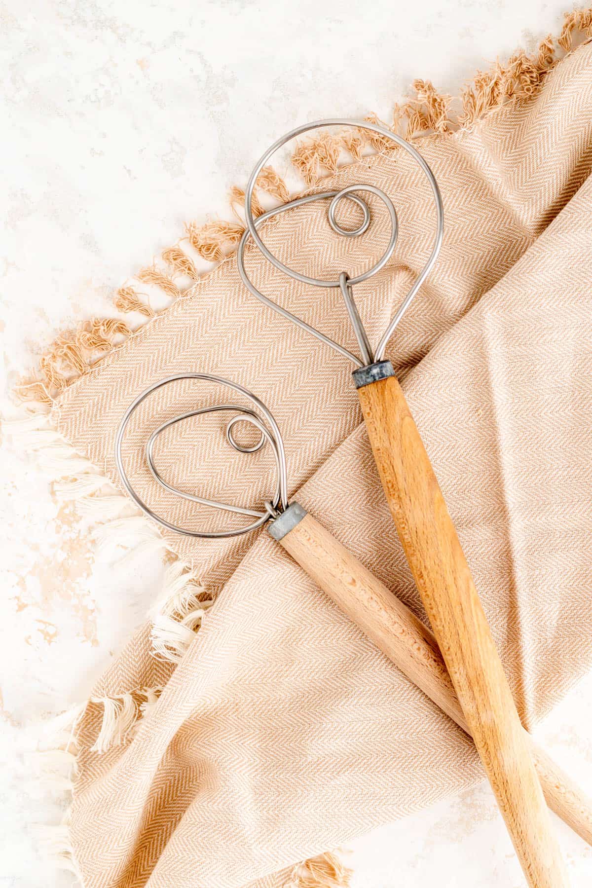 a small and large dough whisk on a brown towel