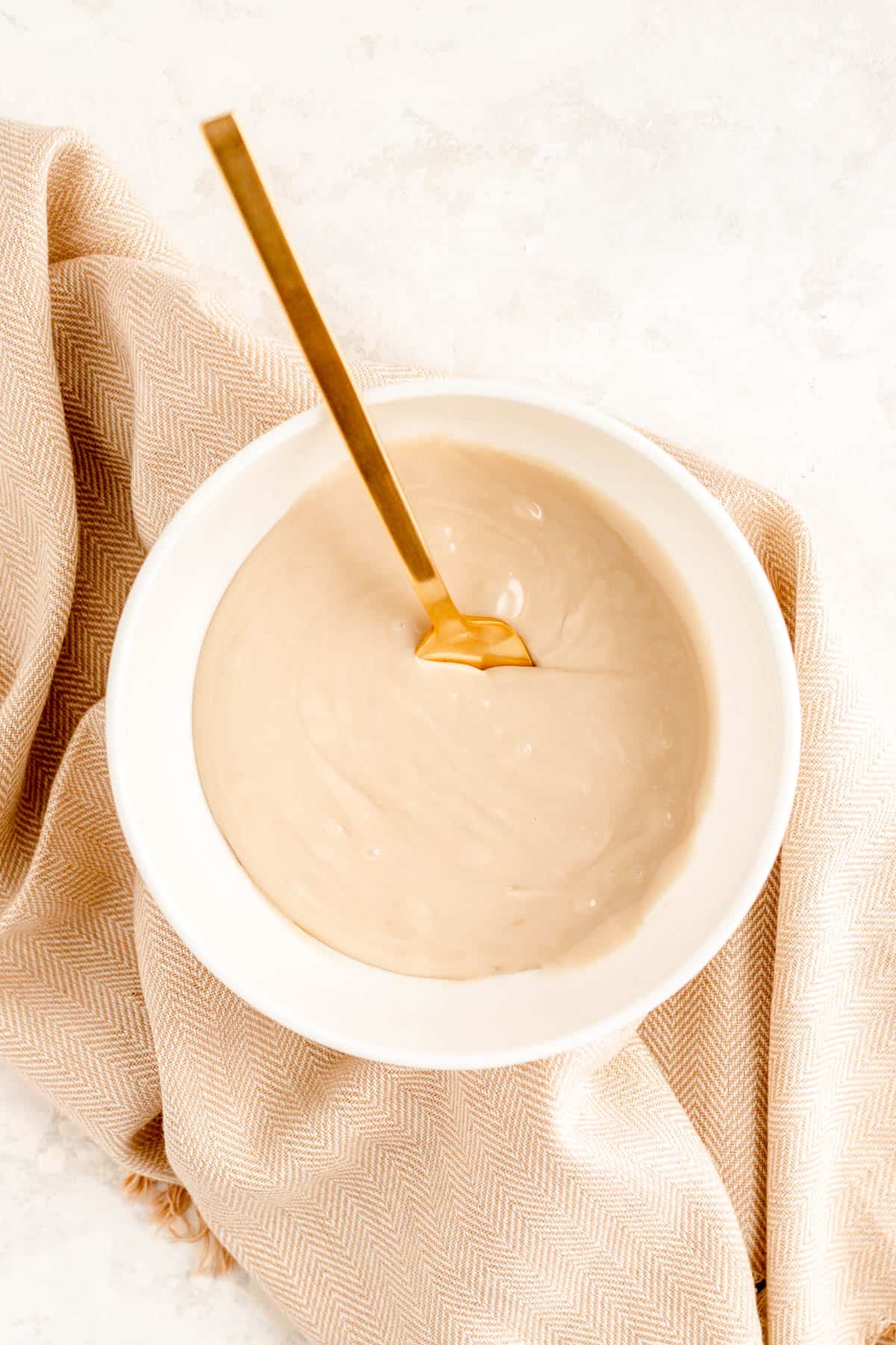 a bowl of maple glaze with a gold fork in it on a brown towel