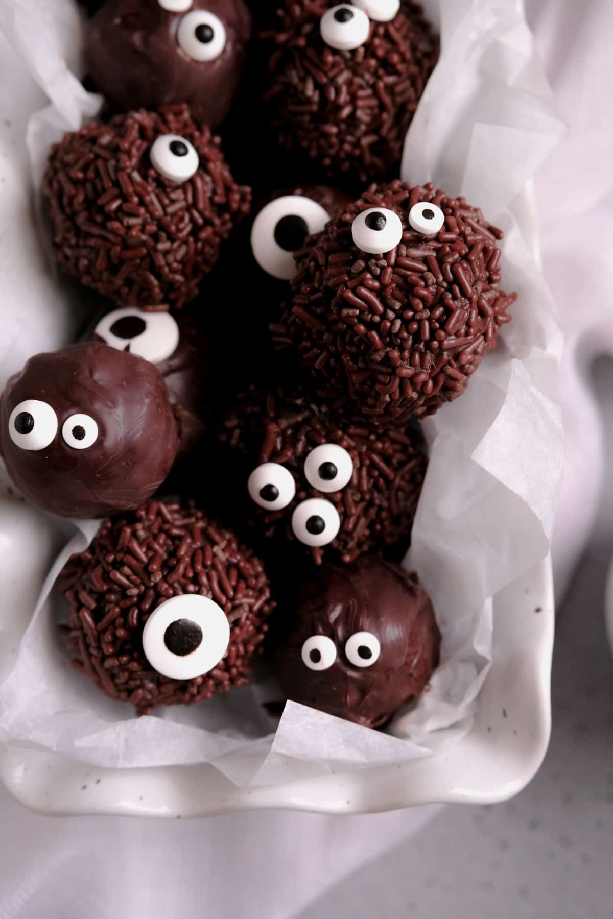 chocolate brownie truffles with sprinkles and candy eyes piled in a white dish
