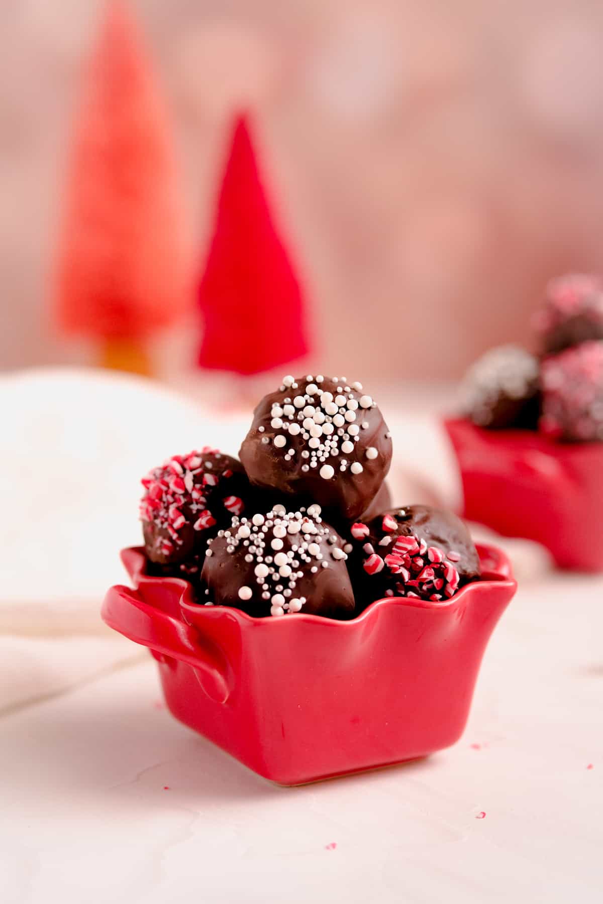 chocolate brownie truffles with holiday sprinkles in a red dish with red Christmas trees in background