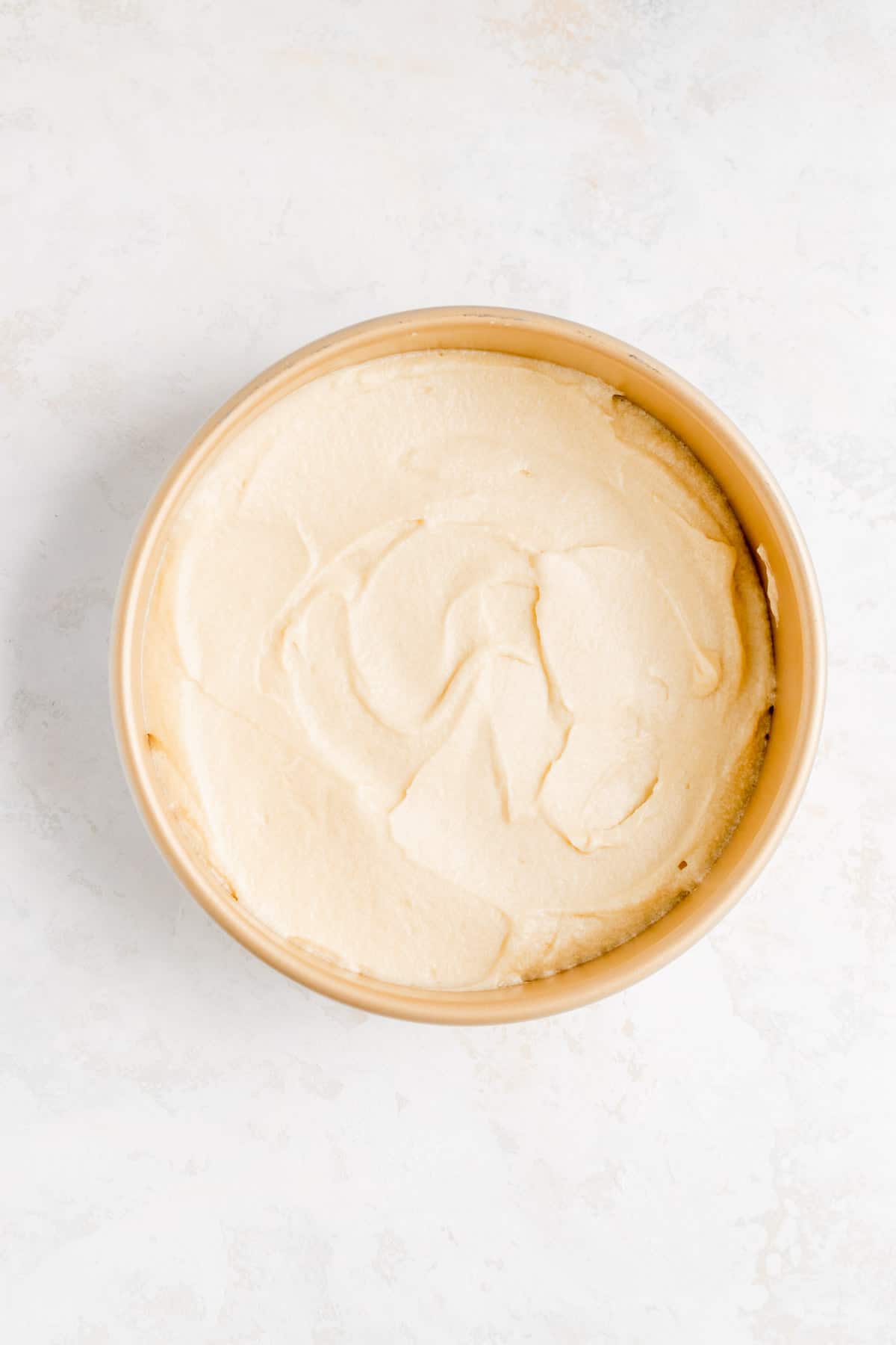 raw cake batter in a gold cake pan on a white background