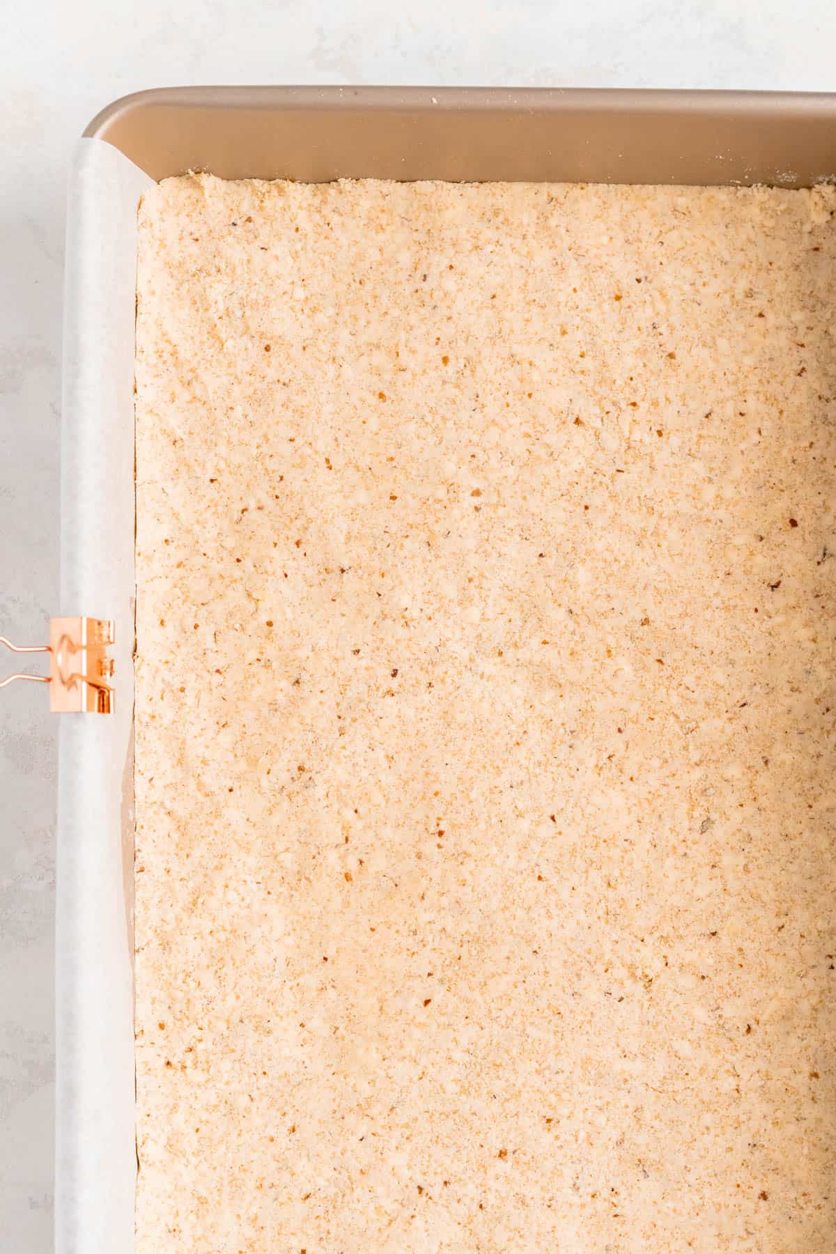 the raw pecan shortbread crust pressed in the bottom of a parchment lined gold pan