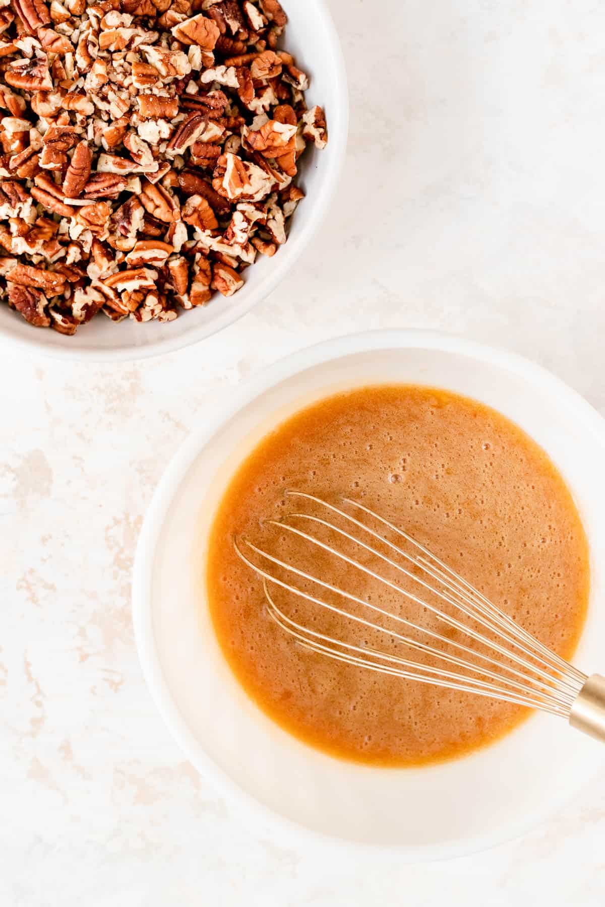 a mixture of wet ingredients in a white bowl with a bowl of pecans next to it.