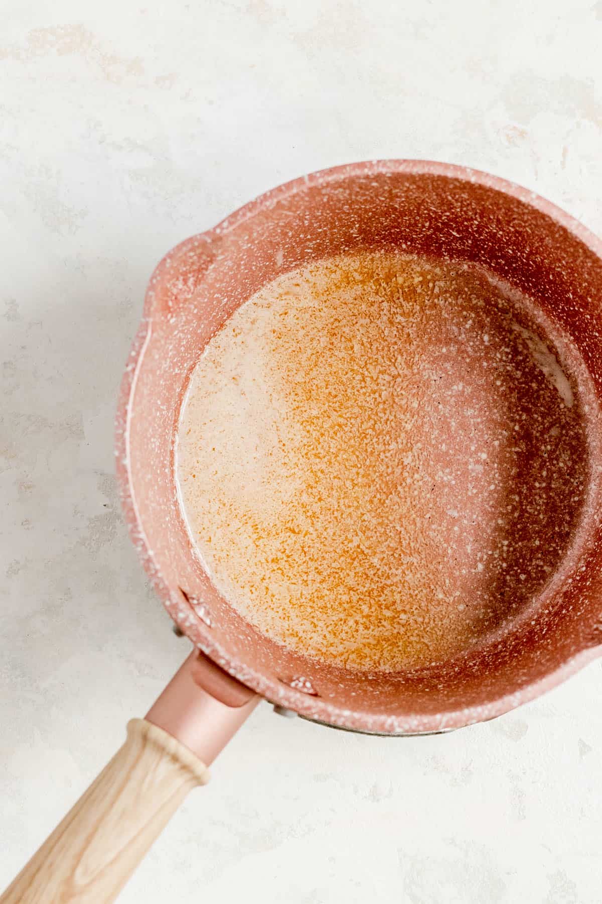 melted butter in a copper pot with white paint flecks and a wooden handle