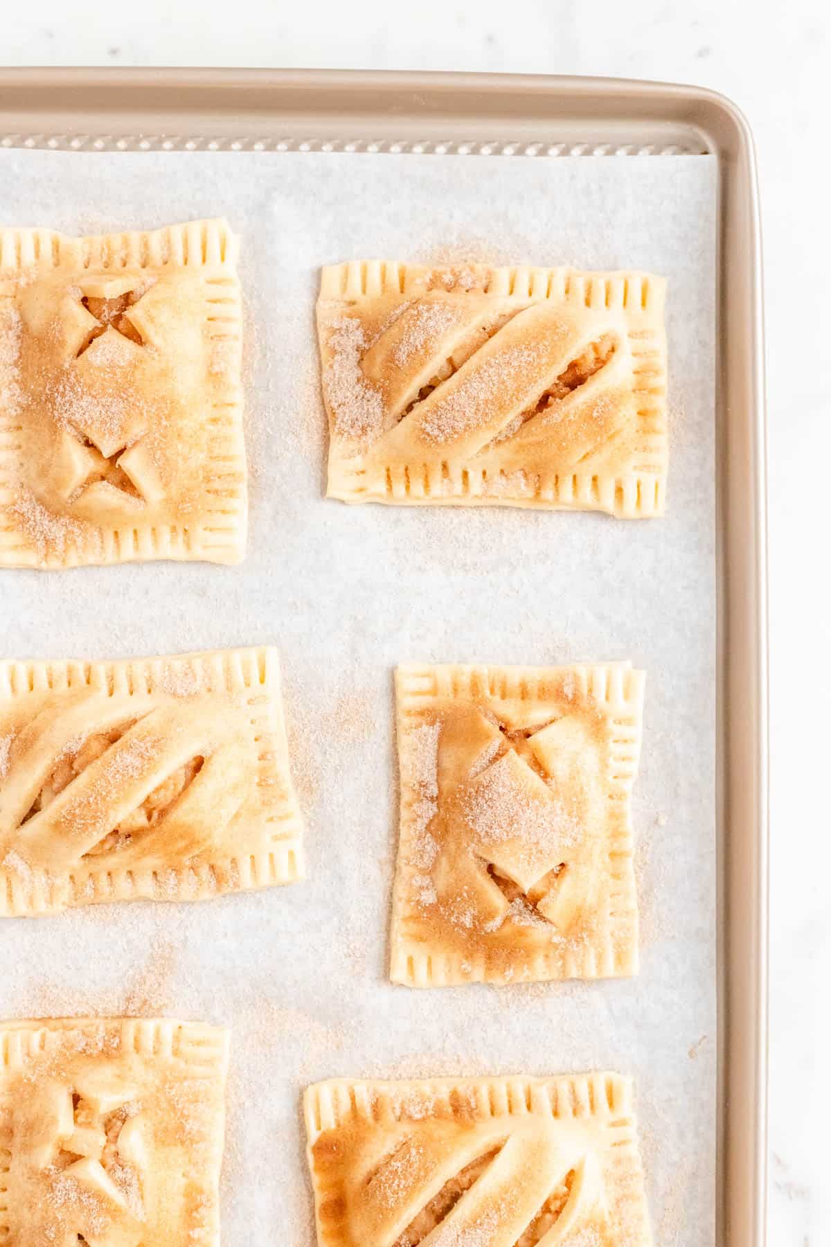 assembled hand pies with cinnamon and sugar on top on a parchment lined gold sheet pan