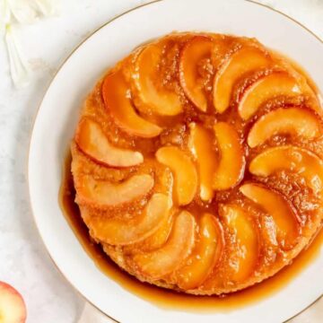 close up of apple cake on a white plate with white mums around it