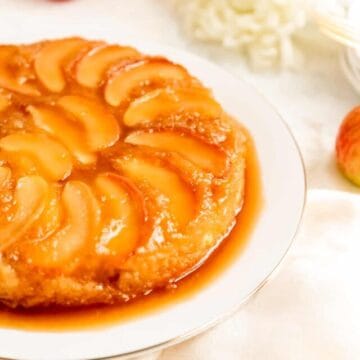 side shot of apple cake on a white plate with white mums and apples