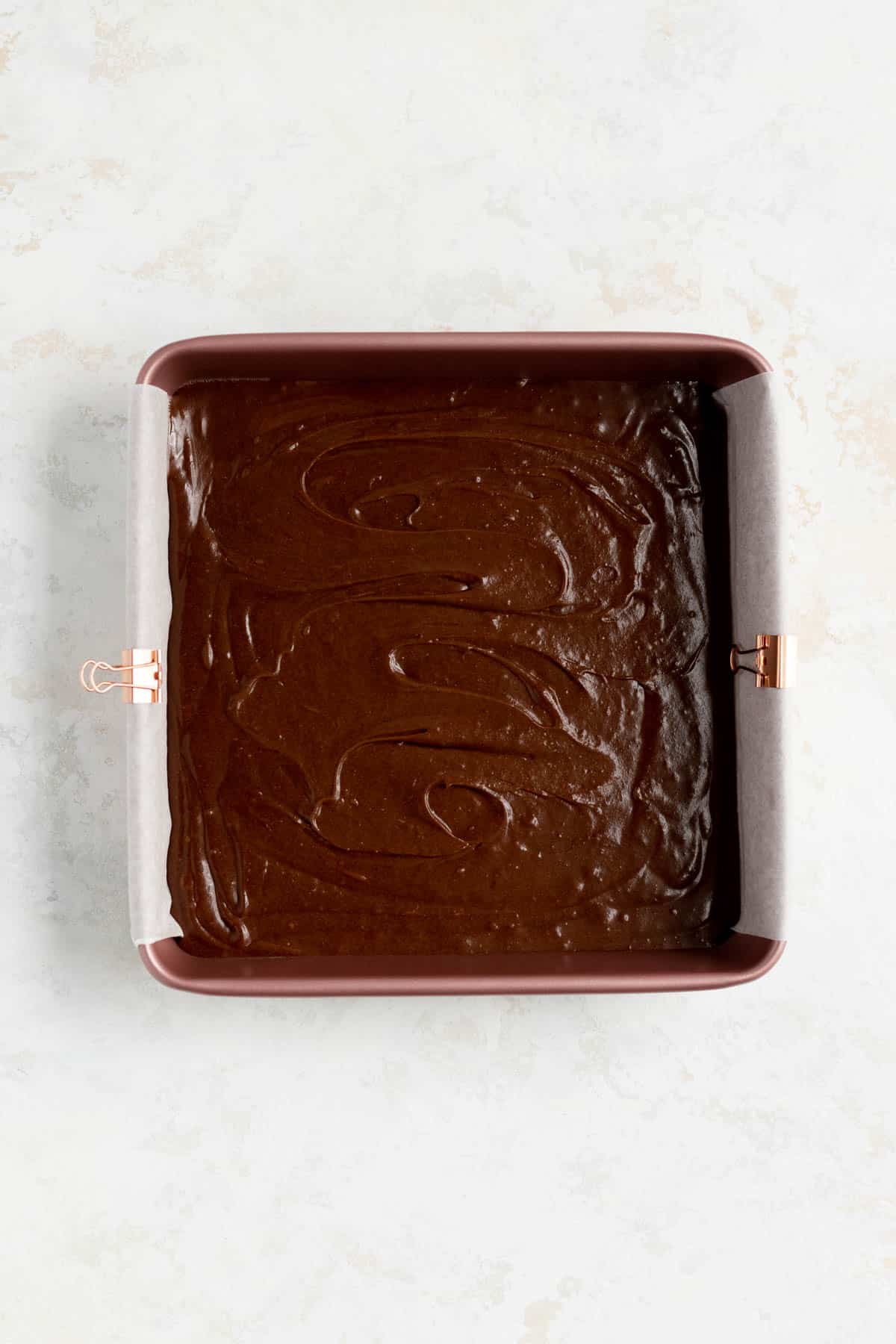raw fudgy brownies in a parchment-lined pink pan on a white background