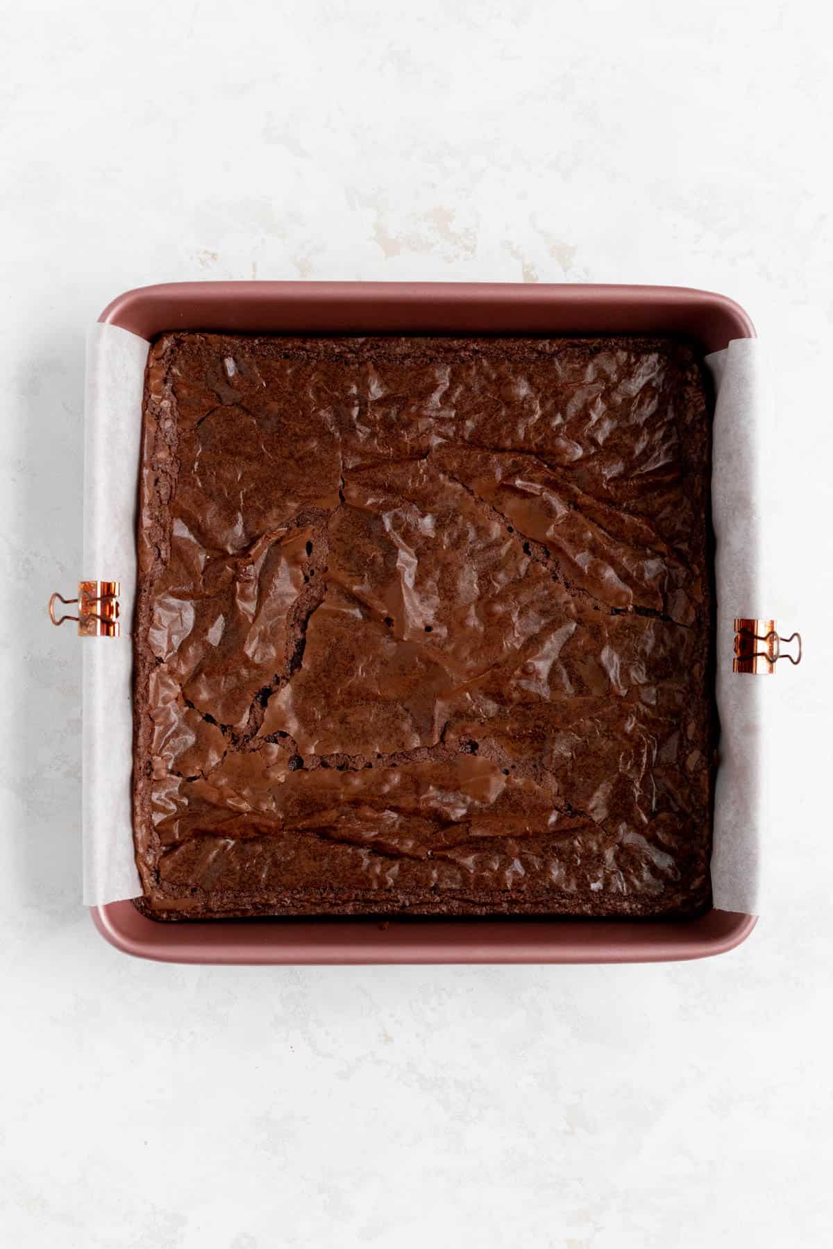 baked fudgy brownies in a parchment-lined pink pan on a white background