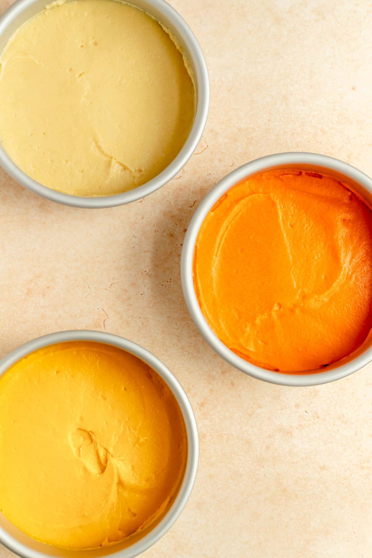 white, yellow, and orange raw cake batter in pans