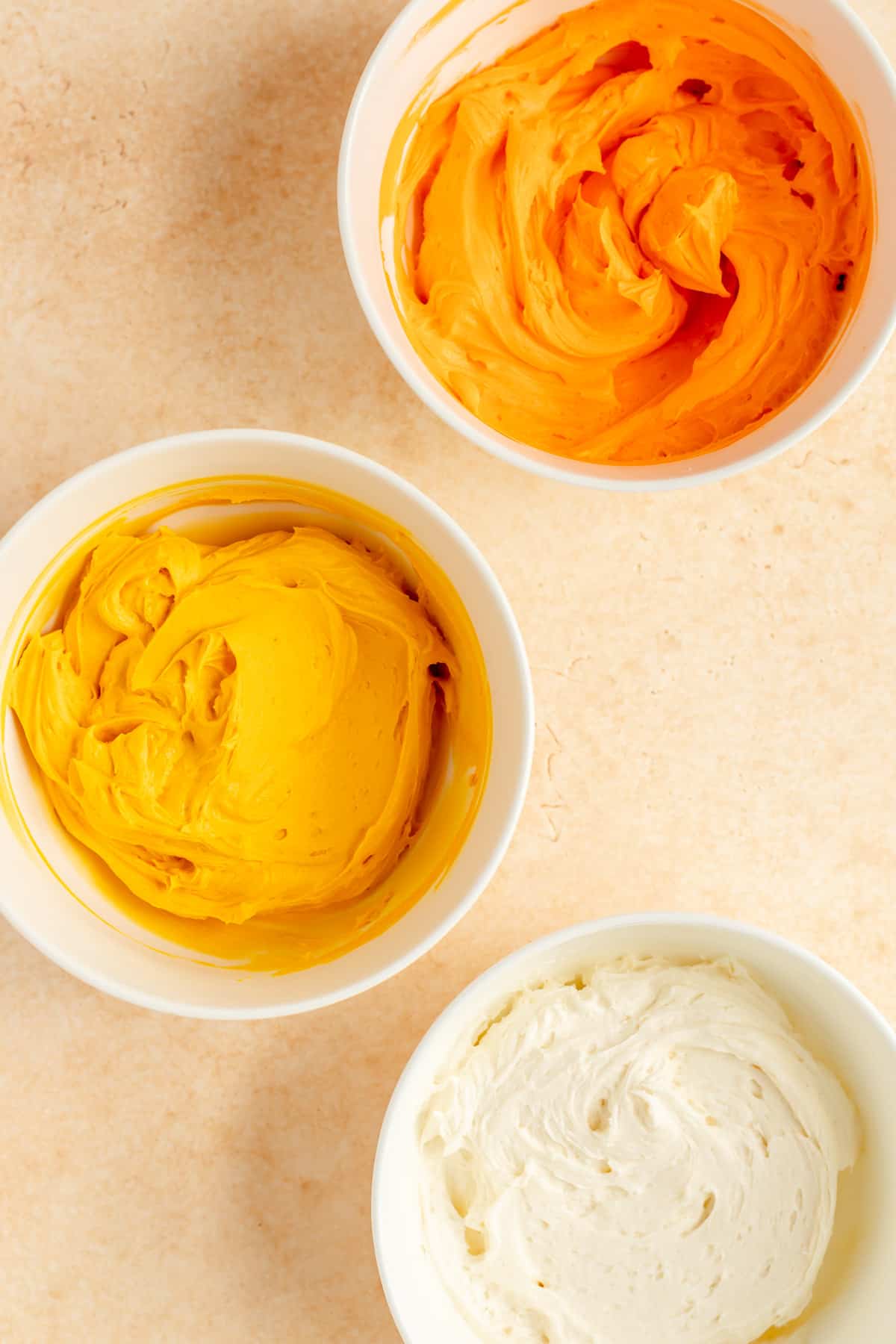 white, yellow, and orange bowls of frosting