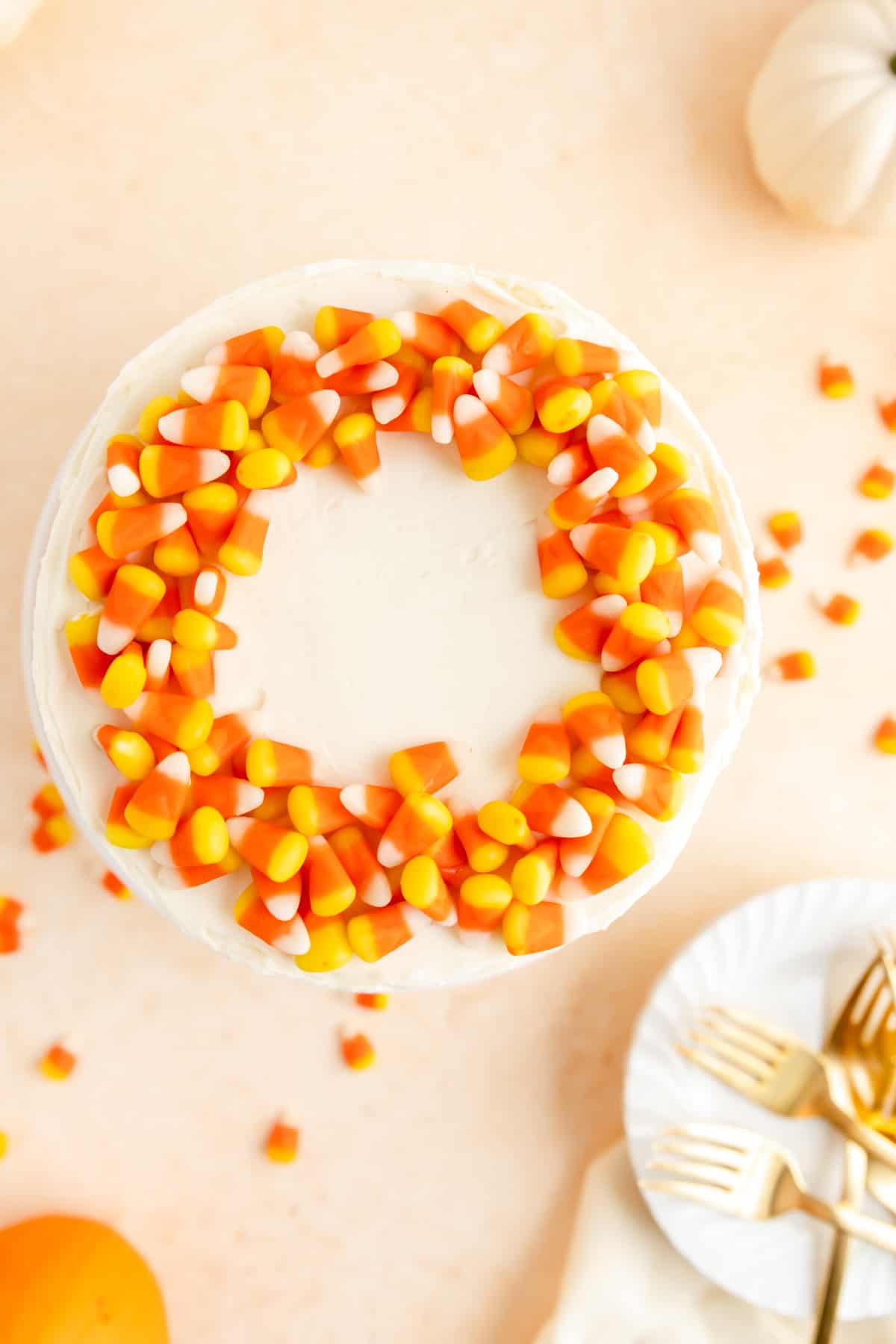 overhead view of candy corn decorated cake with pumpkins, plates, and forks on table