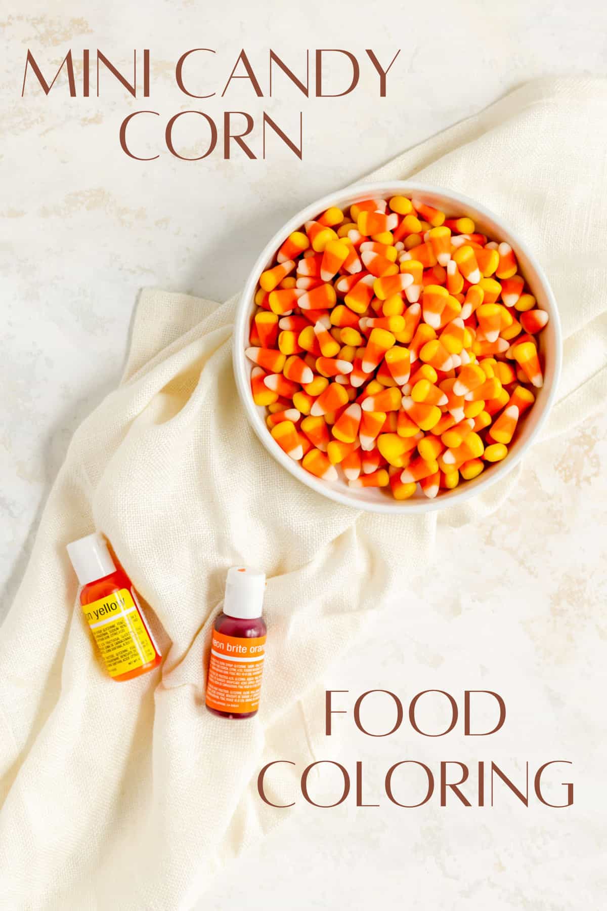 a bowl of mini candy corns and bottles of yellow and orange food coloring on white background