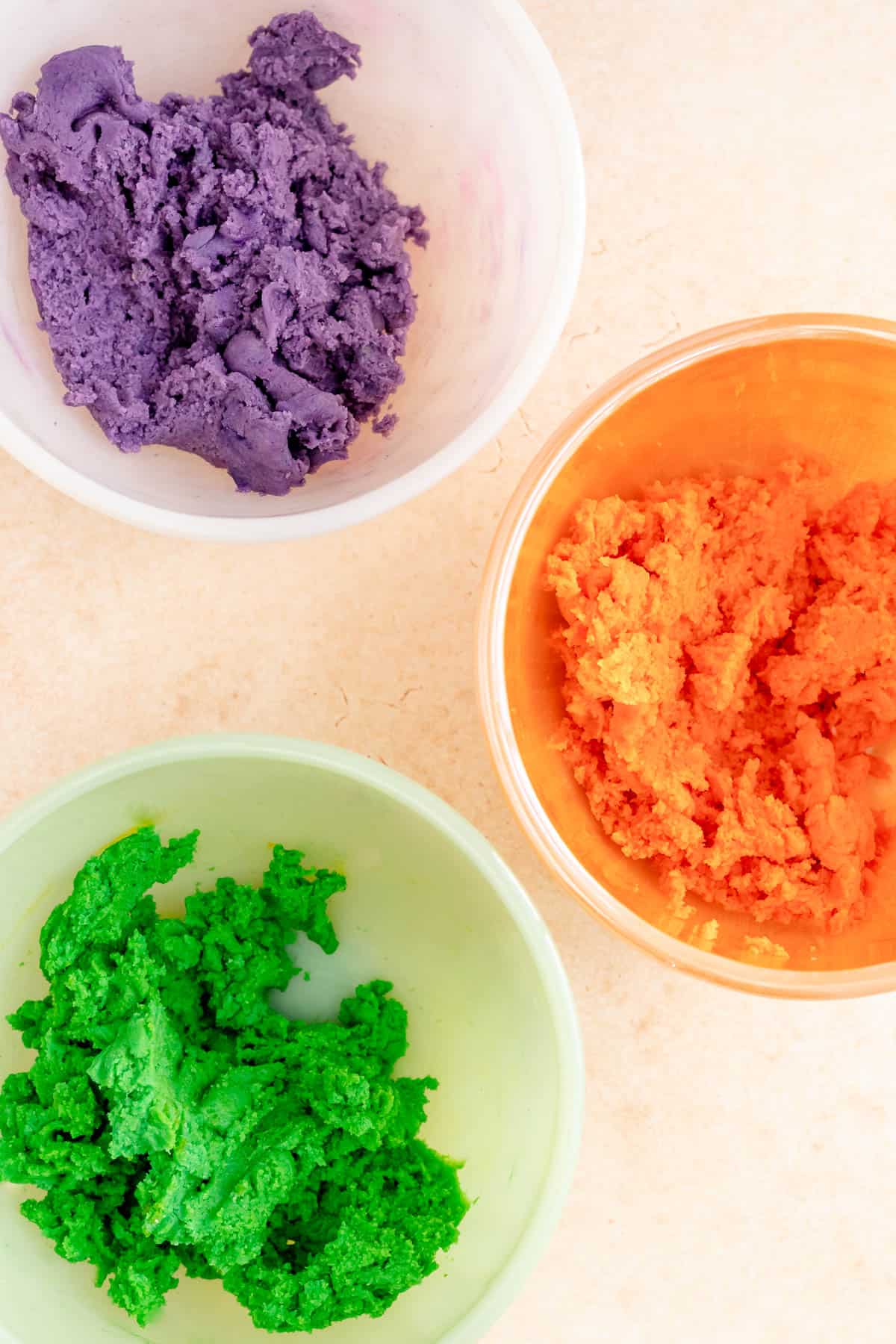 purple orange and green dough in separate bowls