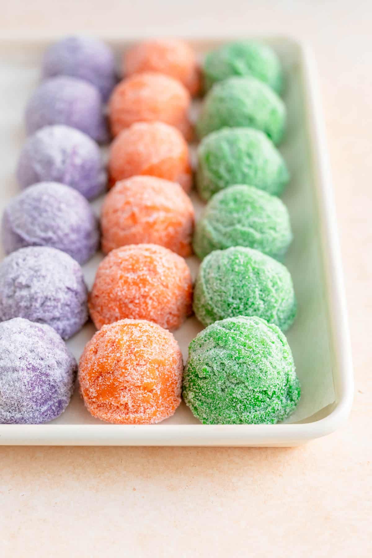 purple orange and green dough balls coated in sugar on a white baking sheet