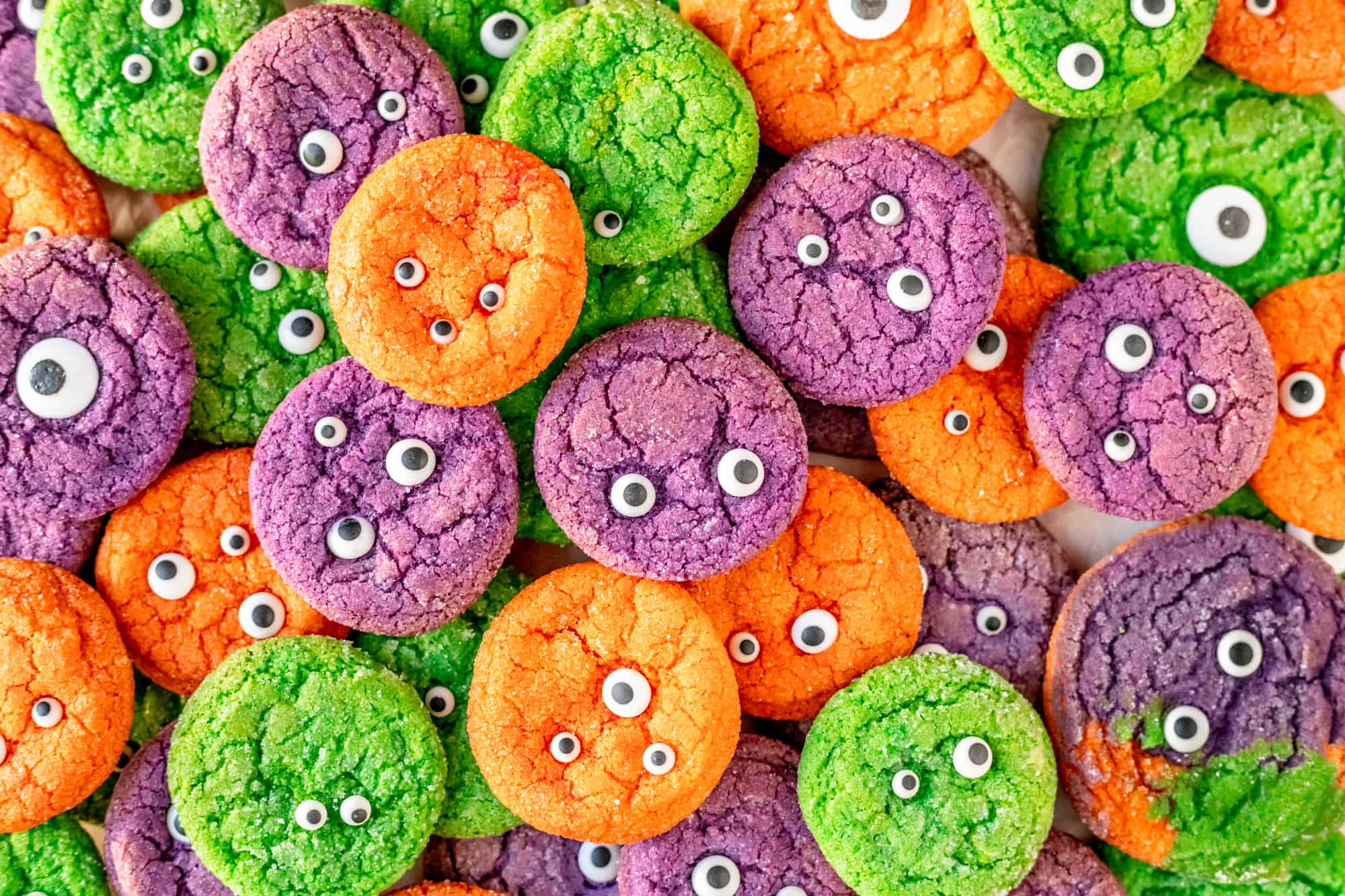 orange purple and green monster sugar cookies with candy eyeballs in a pile
