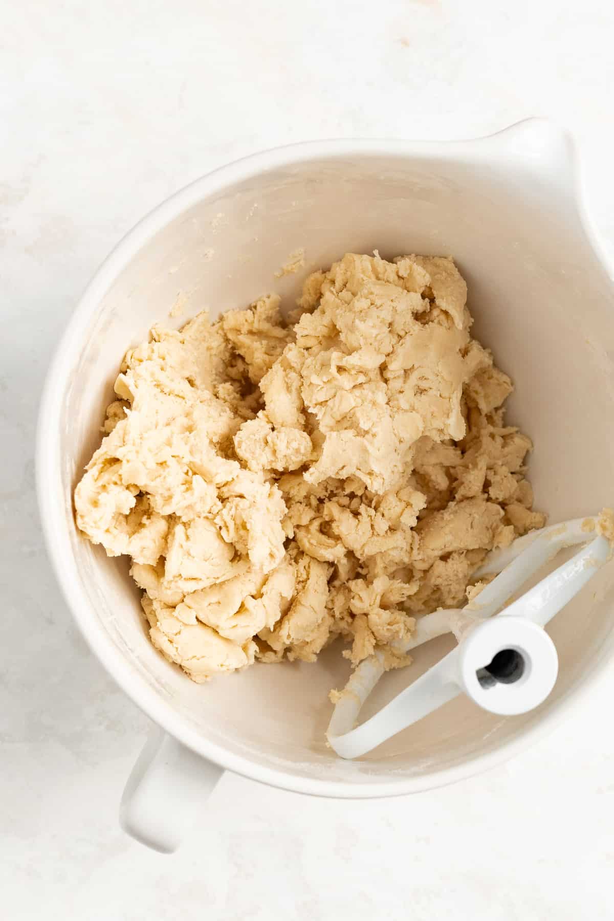 a shaggy mass of mixed pie dough in a white mixing bowl with a white mixer beater