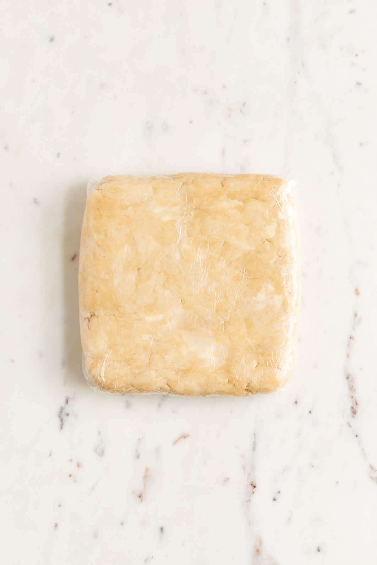 a square wrapped brick of pie dough with butter pieces showing on a marble table
