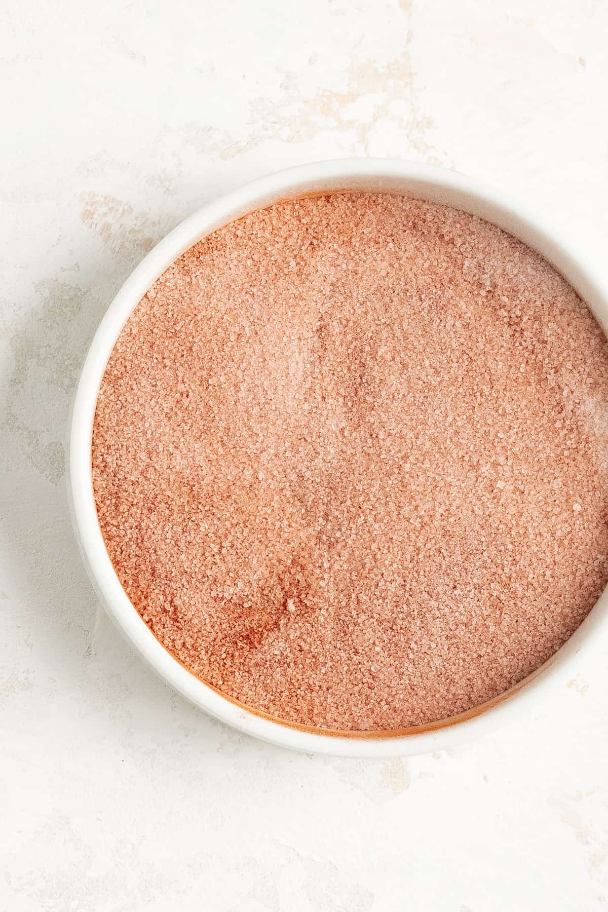 a small white dish with cinnamon and sugar blended in it on a white plaster background