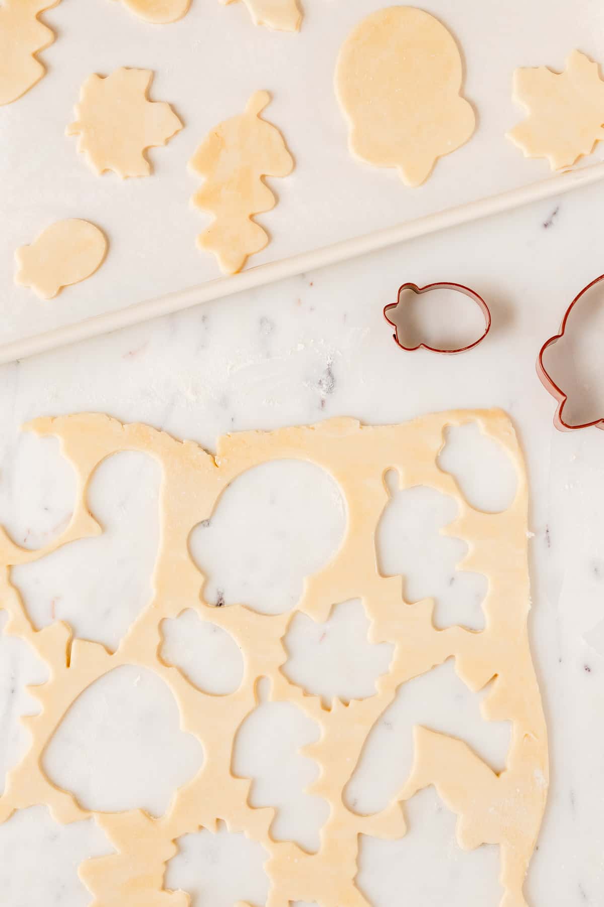pie crust scraps with fall-shaped cut outs and the cut out cookies on a white cookie sheet