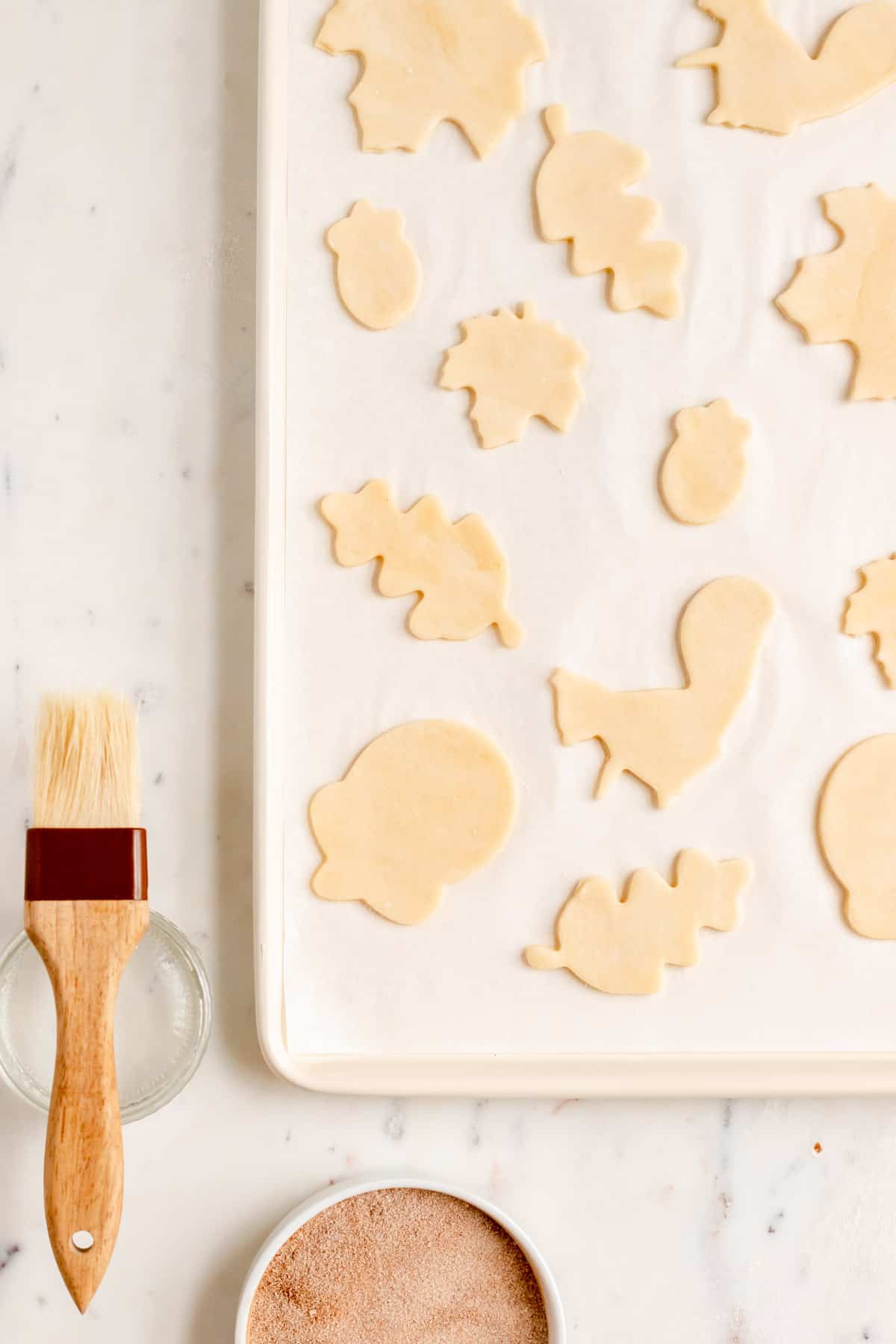 pie crust cookies cut out in fall shapes on baking sheet with brush and topping