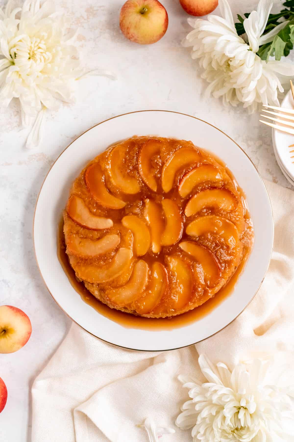 apple cake on a white plate with apples and white mums around it