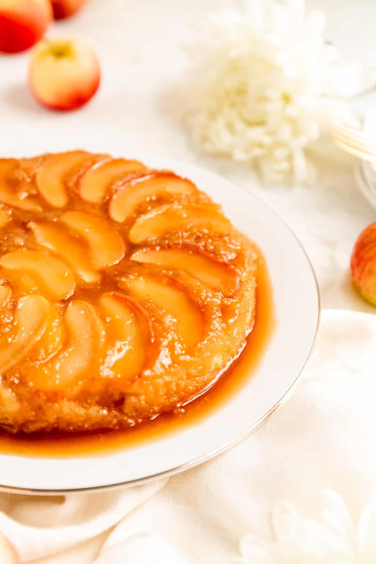 side shot of apple cake on a white plate with white mums and apples