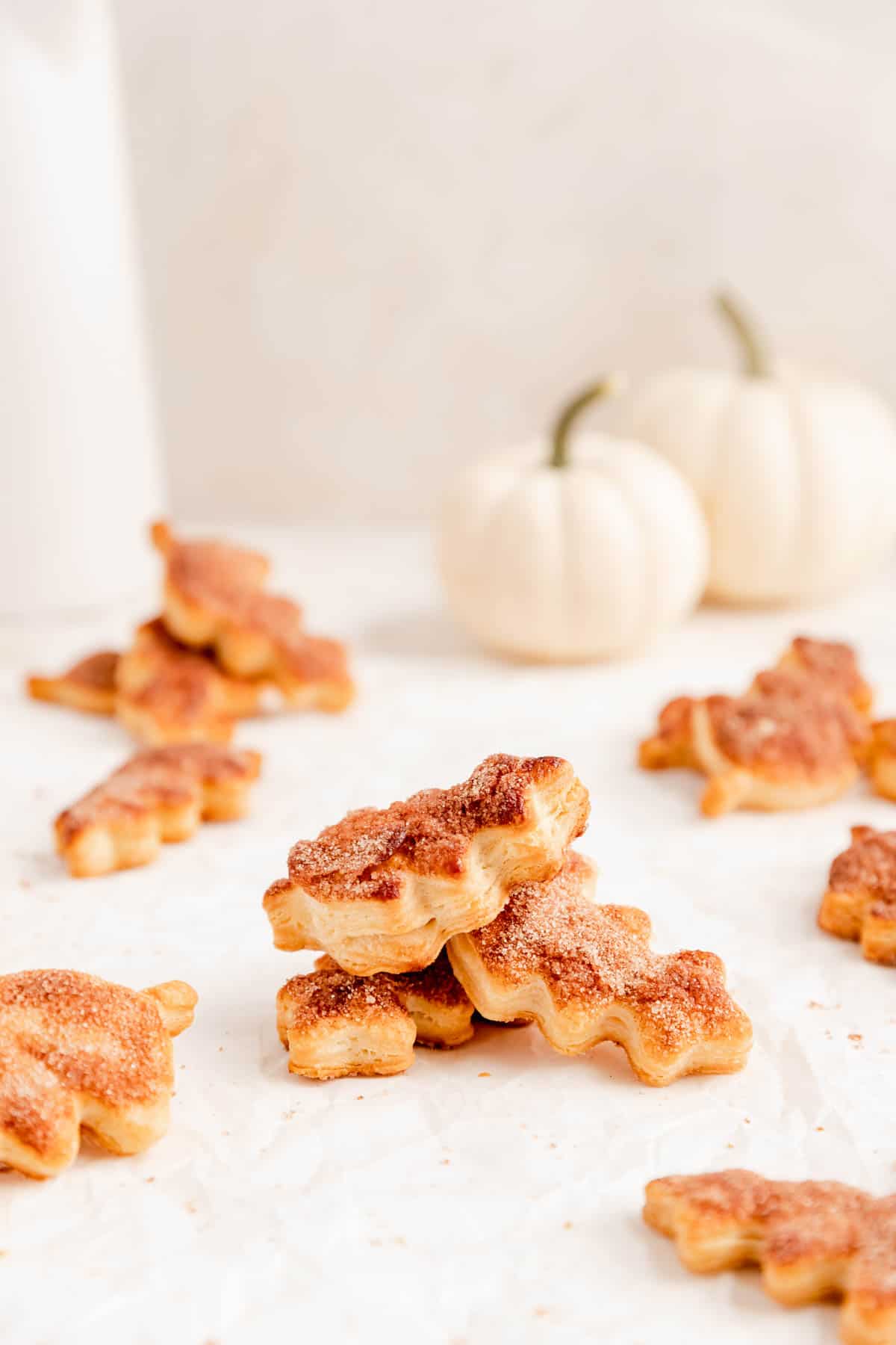 oak leaf pie crust cookies stacked and scattered on parchment with white pumpkins in the background