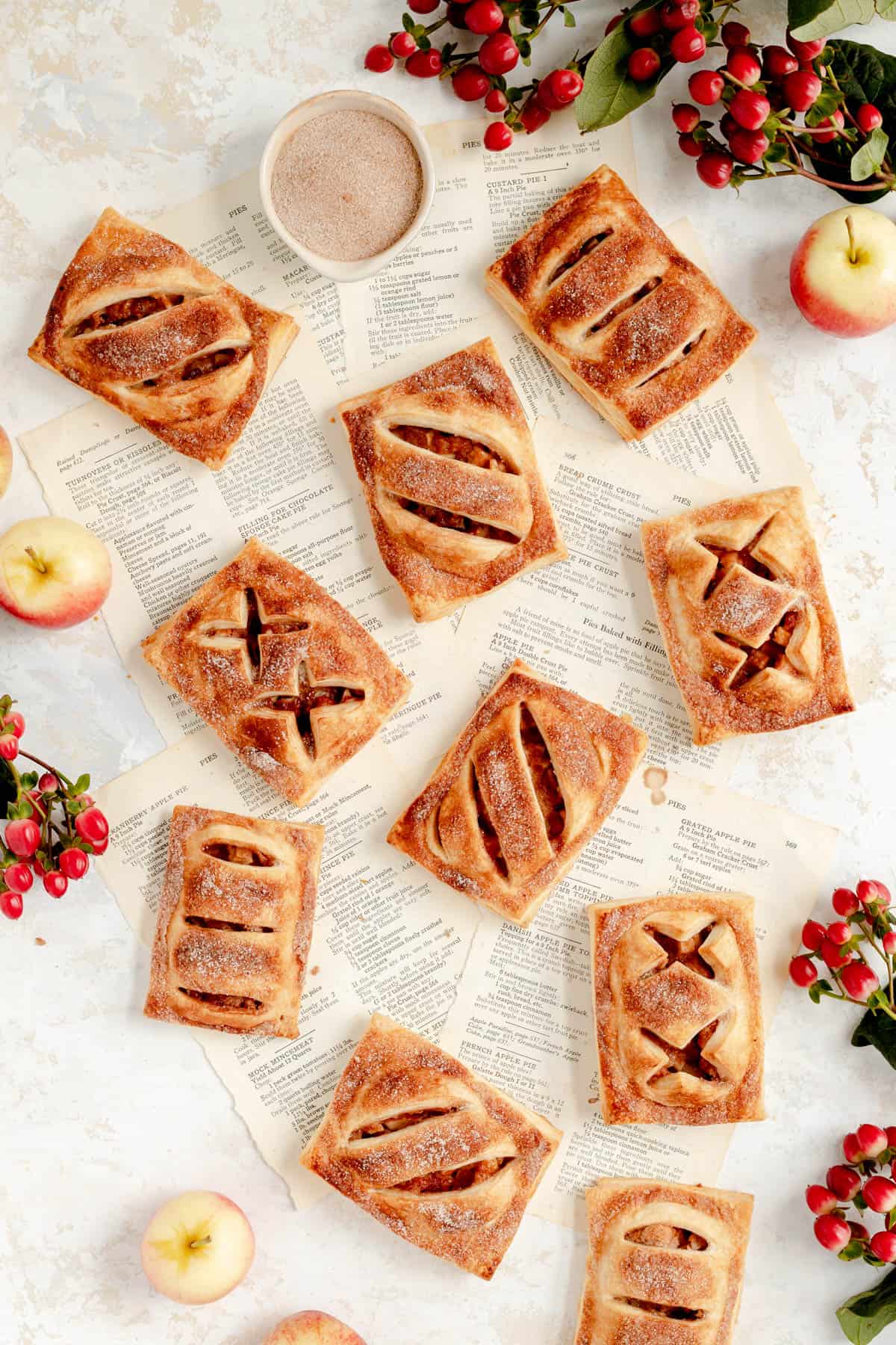a bunch of apple hand pies on torn out recipe pages with red berries and apples