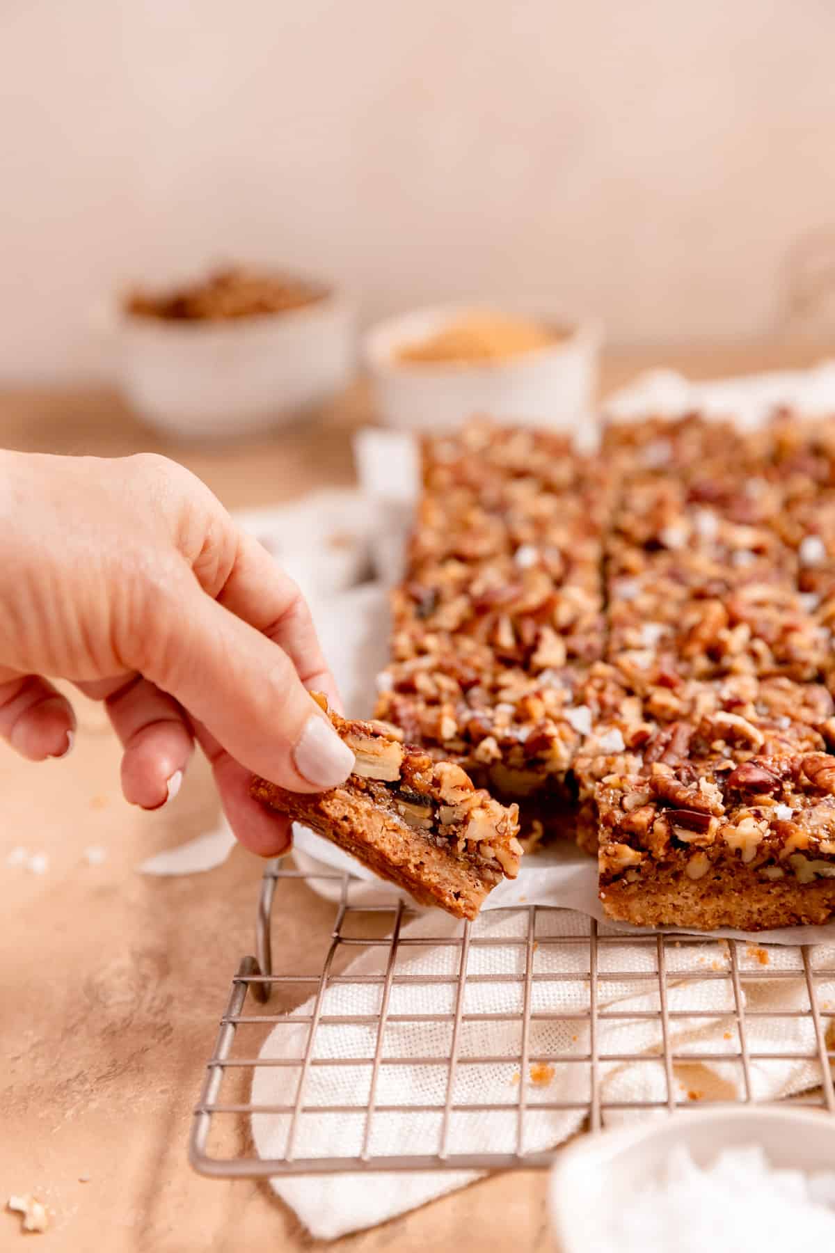 a hand grabbing a piece of pecan pie bars on a gold cooling rack