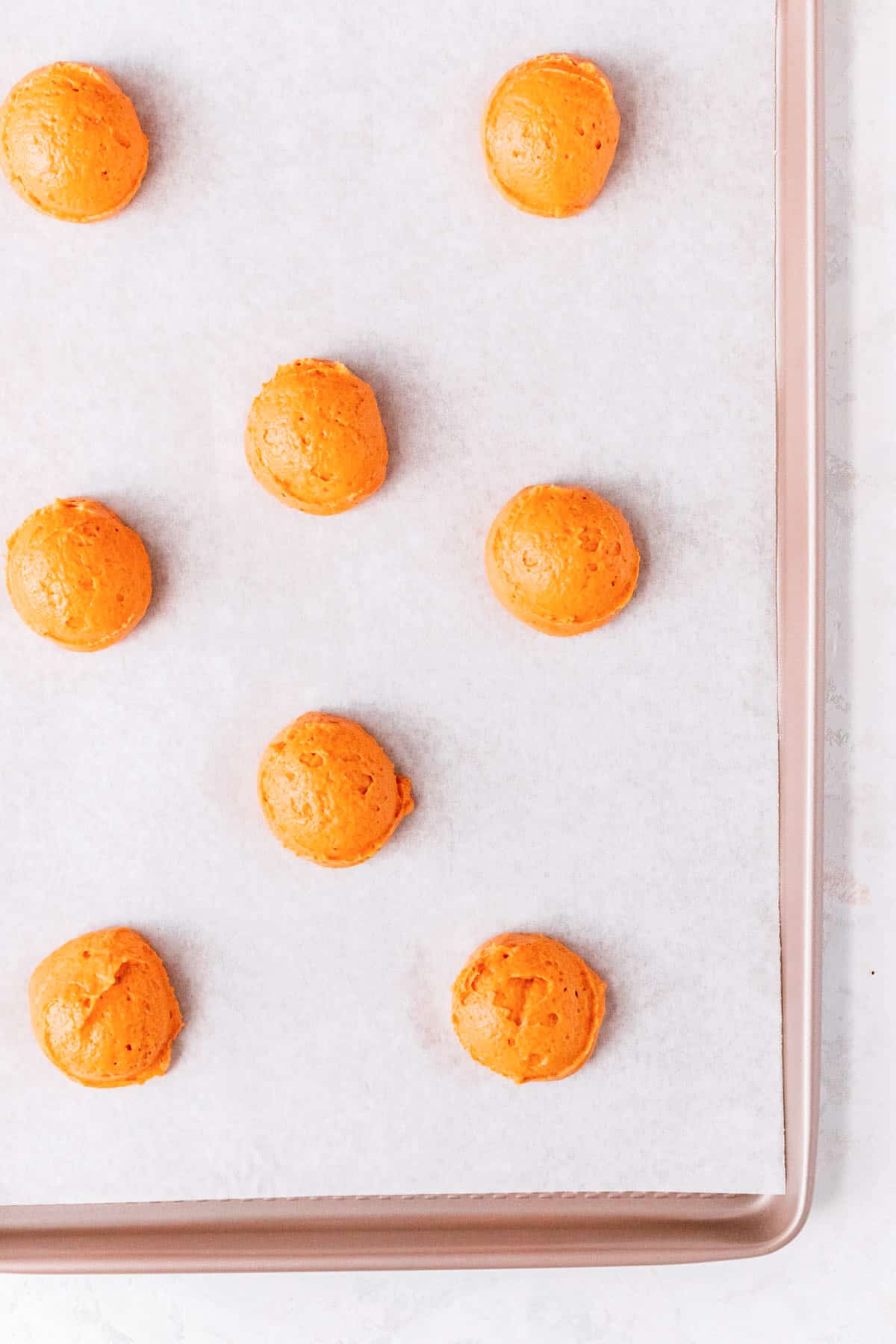 pumpkin whoopie pie batter scooped and dropped on a parchment-lined gold pan