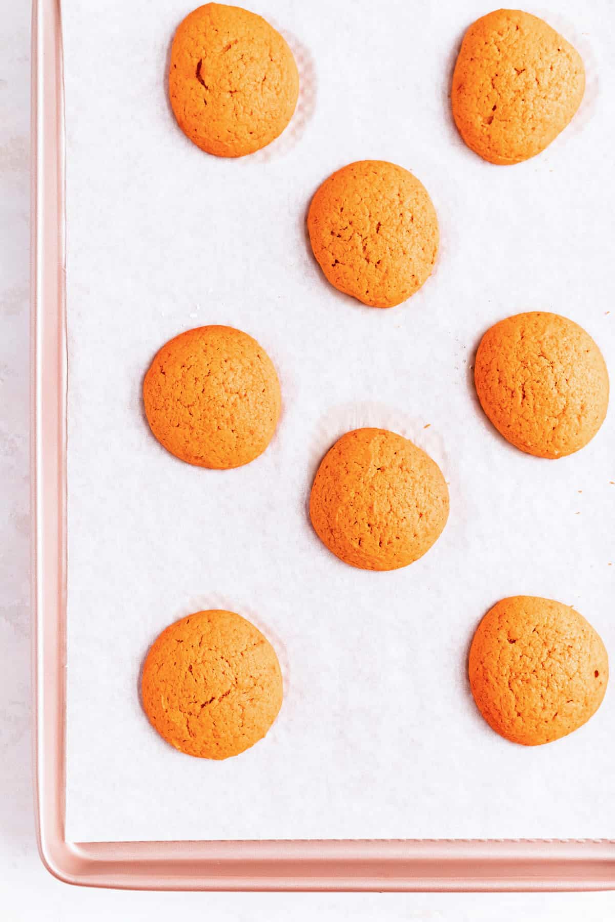 baked pumpkin whoopie pie cookies on a parchment-lined gold pan