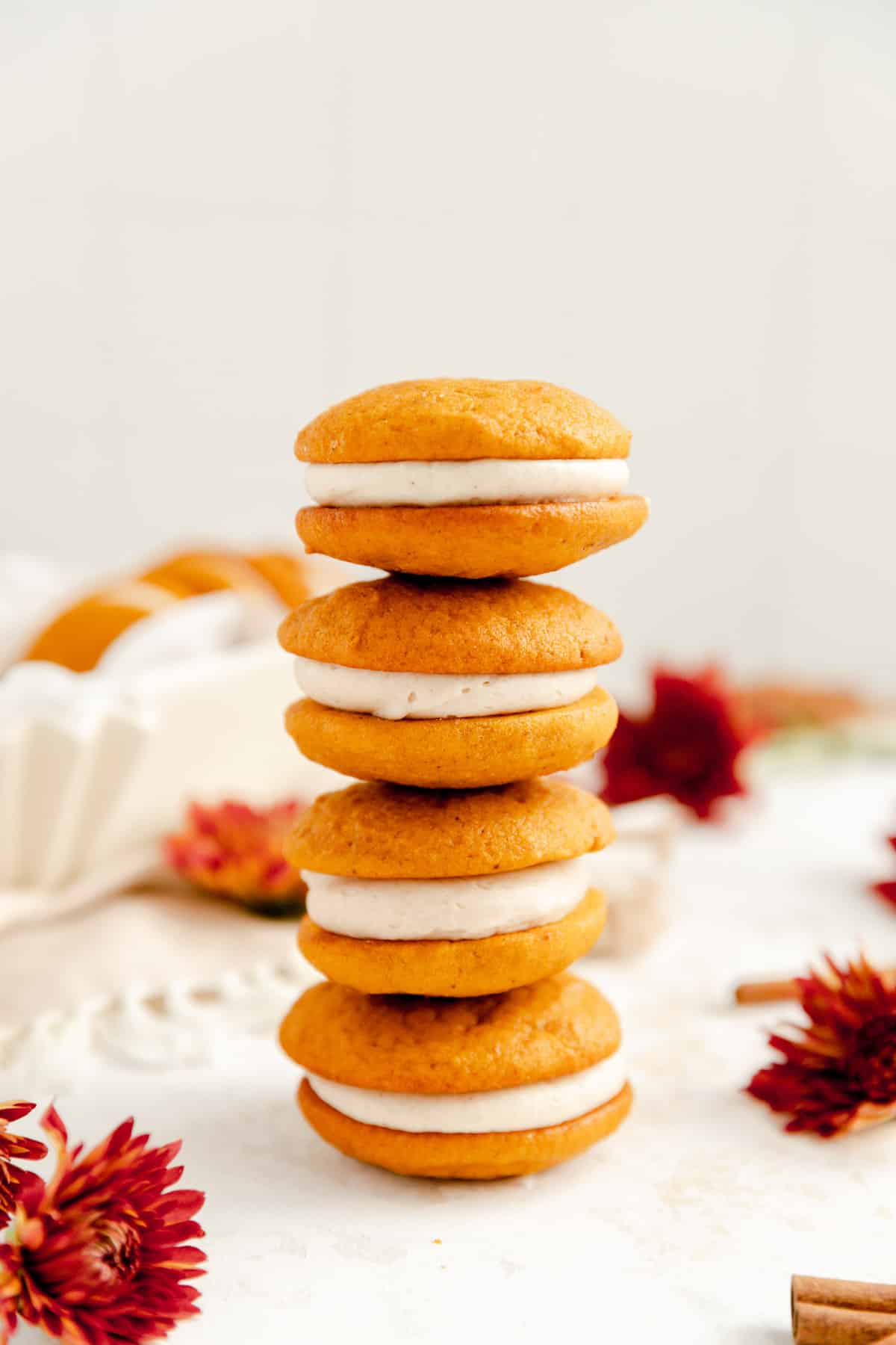 a stack of 4 pumpkin whoopie pies with cream cheese filling surrounded by red mums