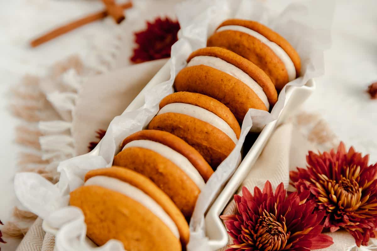 a long white dish filled with five pumpkin whoopie pies with rust colored mums