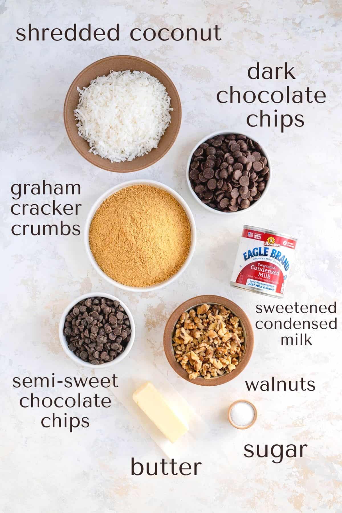 labeled ingredients in individual bowls for seven layer magic bars