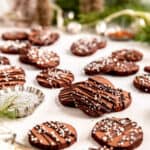 chocolate butter cookies with chocolate drizzle and white sprinkles scatter on a table with evergreen branches