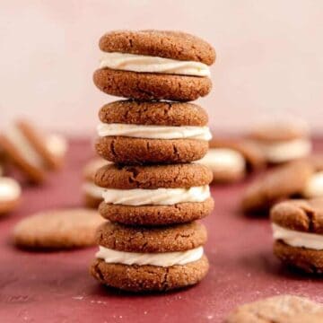 A stack of four ginger sandwich cookies and a burgundy surface with other cookies on the table