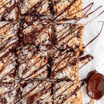 Seven layer cookie bars drizzled in melted chocolate with a chocolate covered gold spoon on side